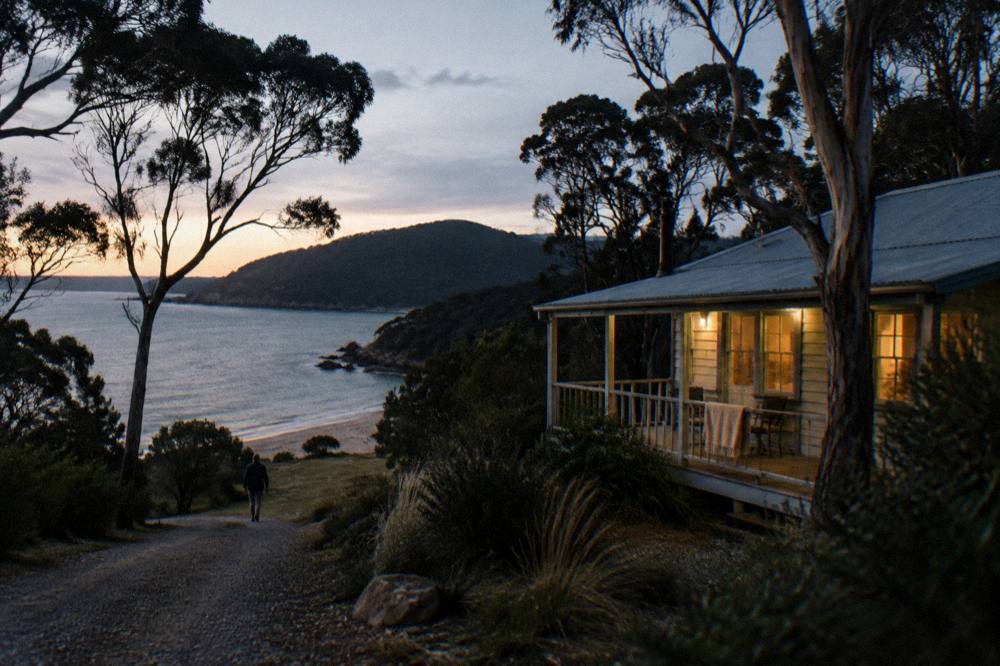 Cottage windows glowing at dusk above a darkening bay